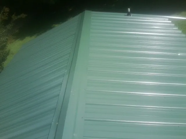 New green metal panels meeting at the ridge of a roof — Flat Roof Repair work by our crew in Springdale