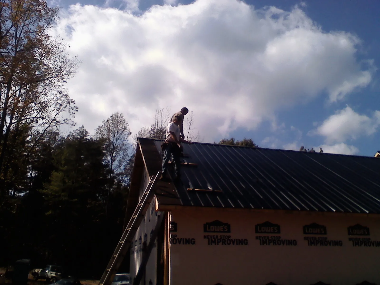 Roofer fastening dark metal panels high against a cloudy sky, from a Roof Inspection job in Springdale