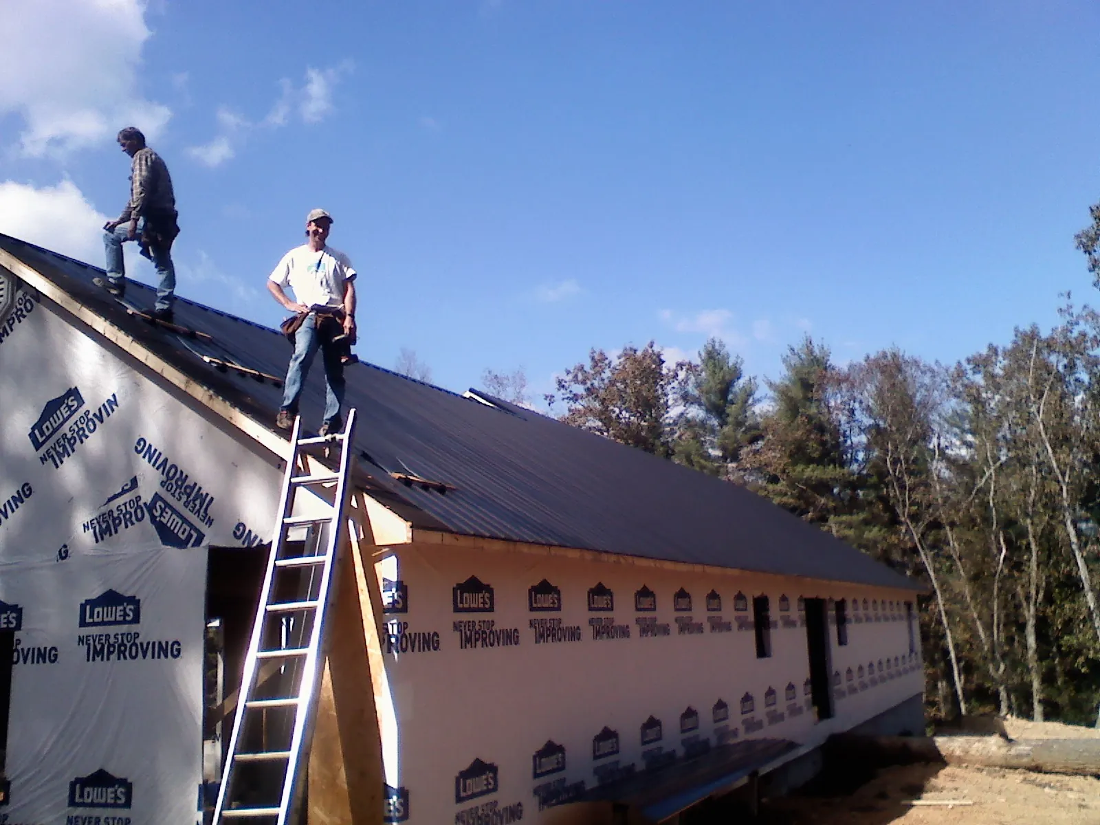 Two roofers standing on a long dark metal roof over a wrapped building in Springdale